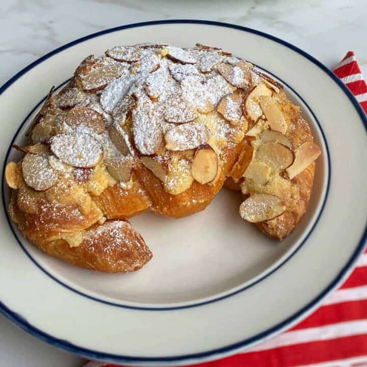 An Almond Croissant dusted with icing sugar sitting on a white plate.