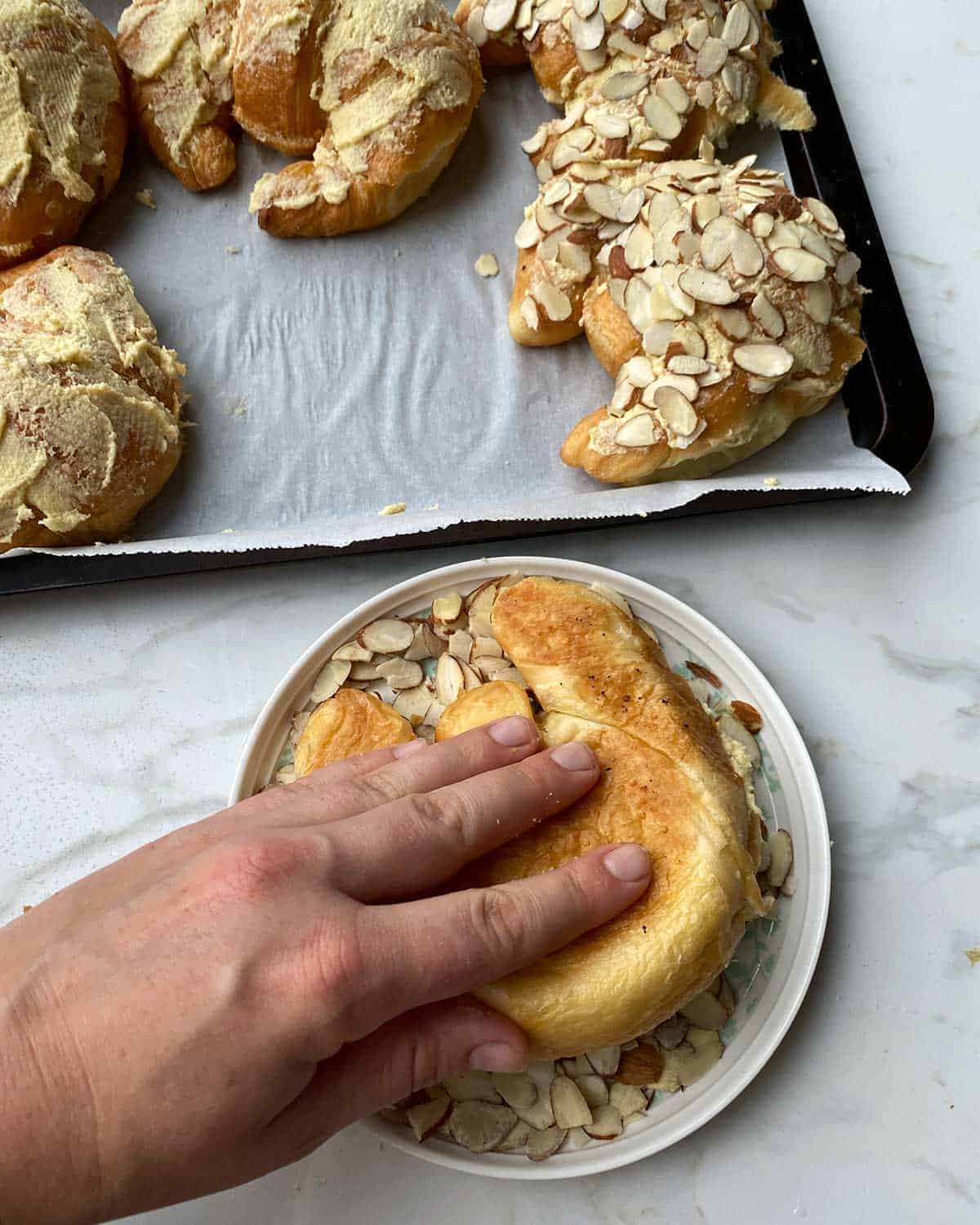 A croissant being dipped in slivered almonds before going on a baking tray.