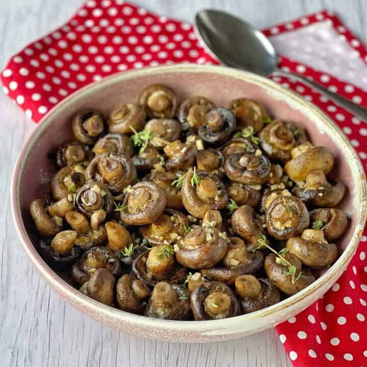 A bowl of Baked Garlic Mushrooms sitting on a red spotty napkin.