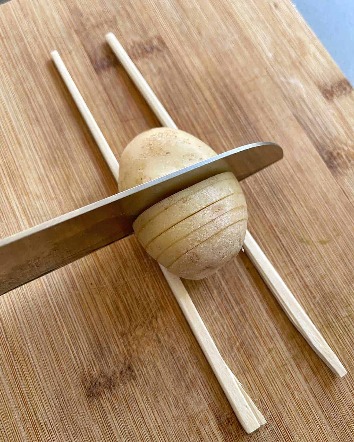 A potato being cut while sitting on two chopsticks.