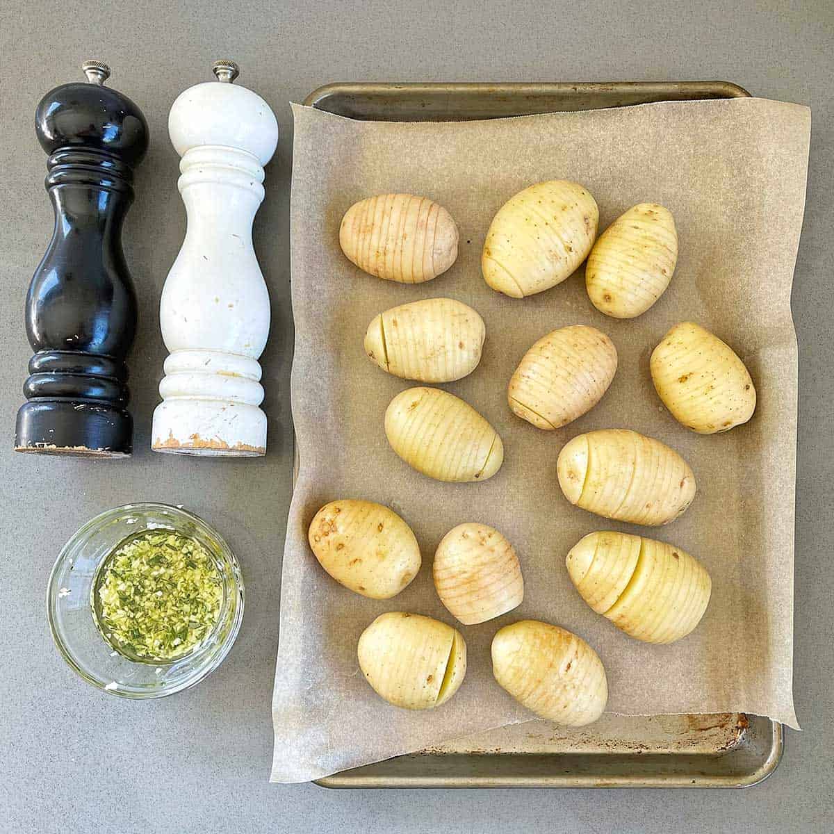Sliced potatoes sitting on a lined baking tray next to salt and pepper grinders.