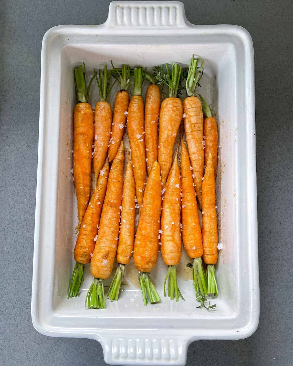 Uncooked carrots in a white baking dish.