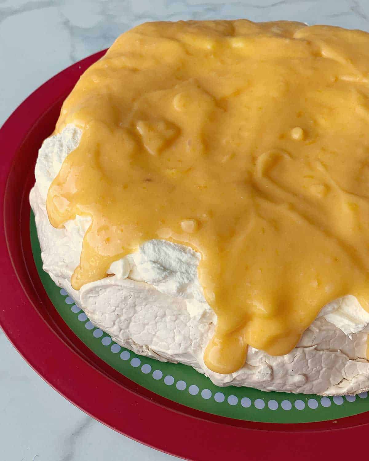 A pavlova topped with cream and lemon curd on a red circular tray.