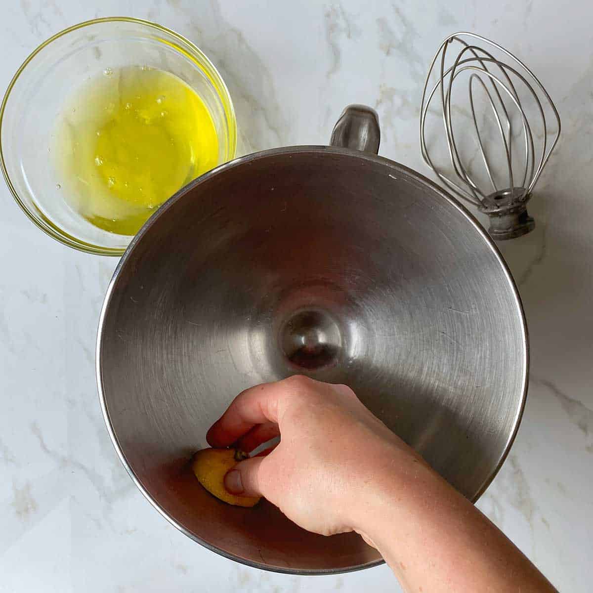 A hand cleaning a mixing bowl by rubbing half a lemon around it.