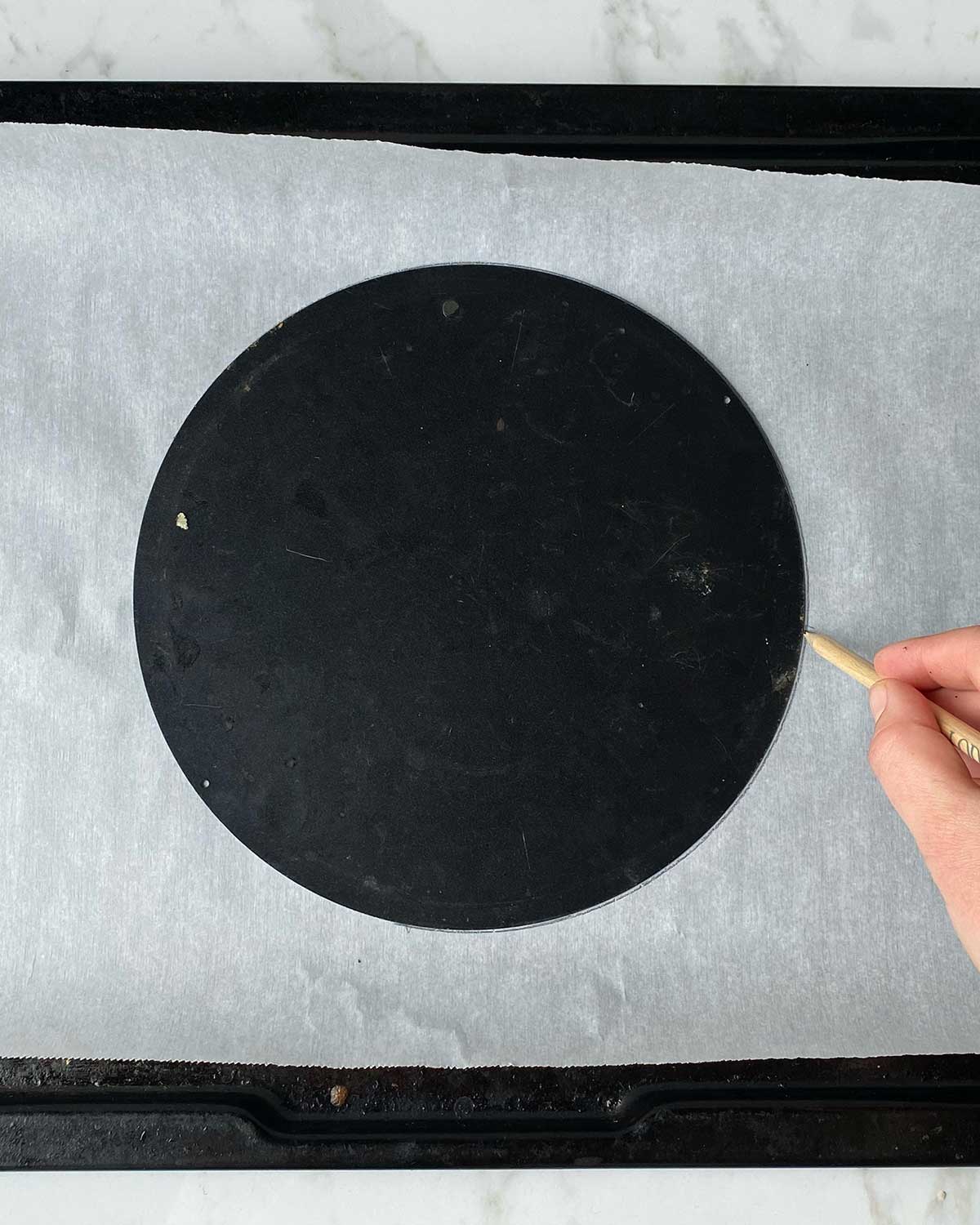 A hand drawing a circle around the base of a cake tin on to baking paper.