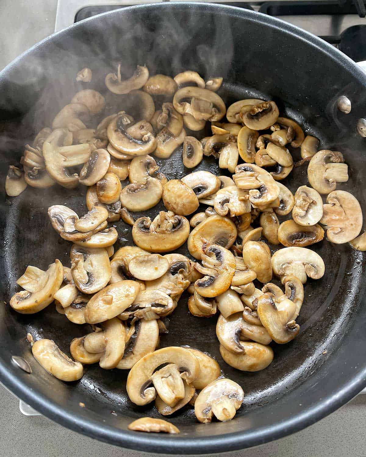 Sliced mushrooms cooking in a frying pan.