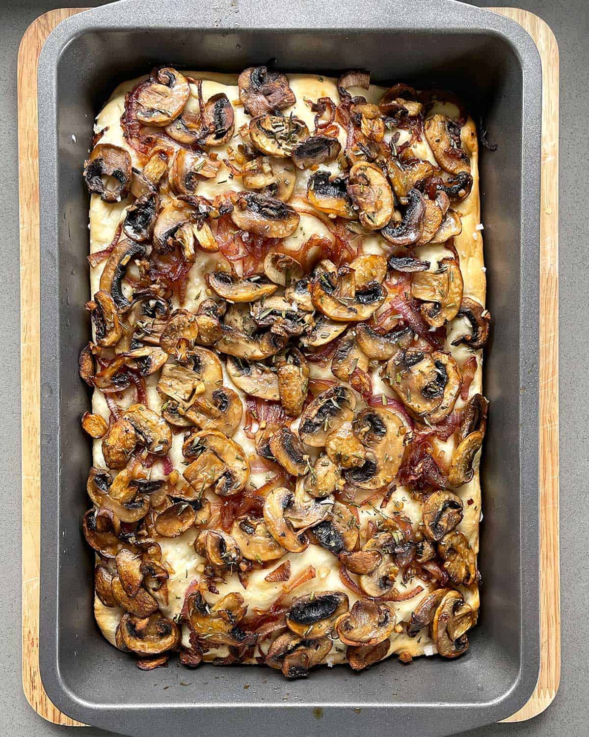 Cooked mushroom focaccia in a baking tray on wooden chopping board.