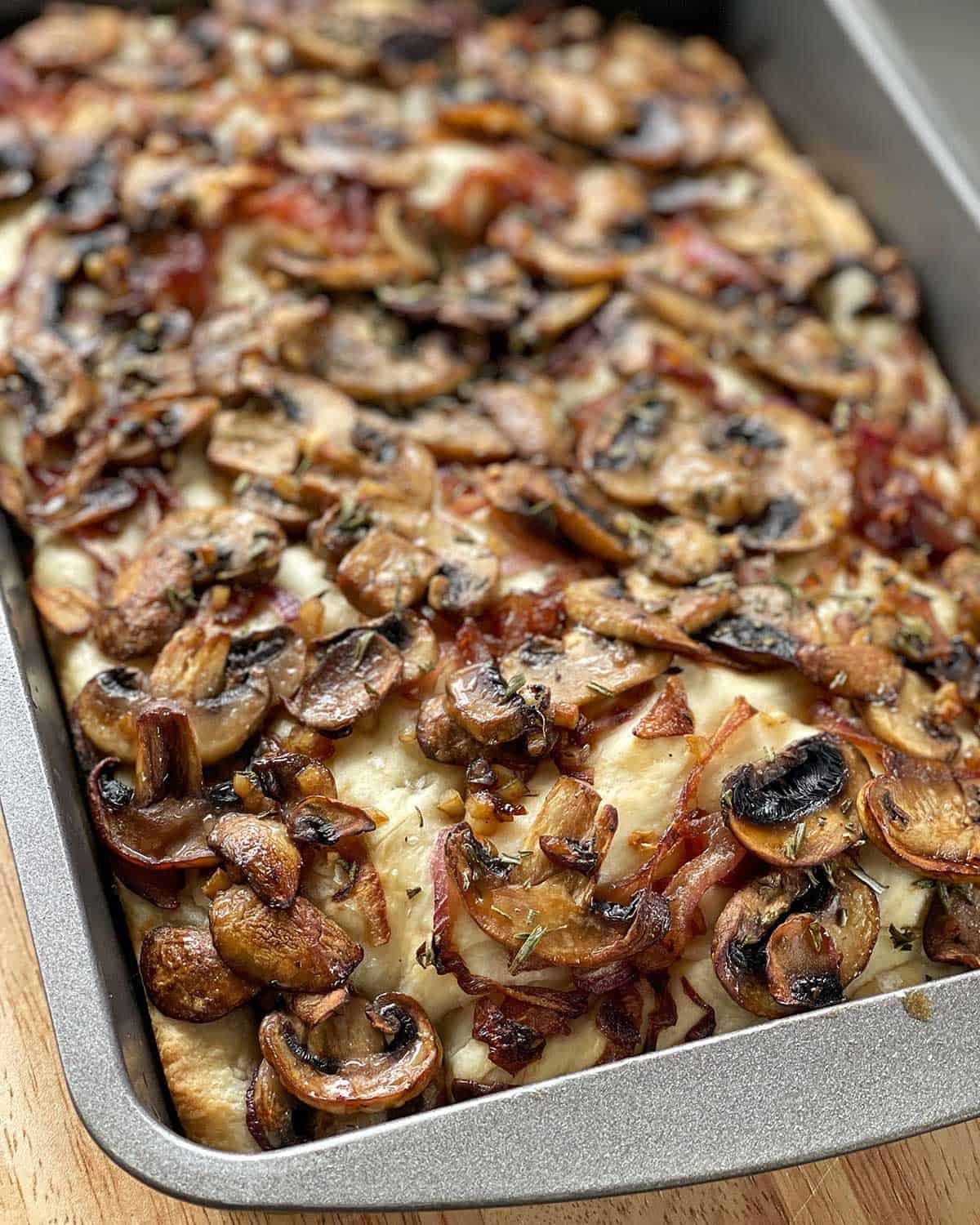 A close up of a cooked Mushroom Focaccia in a grey baking dish.