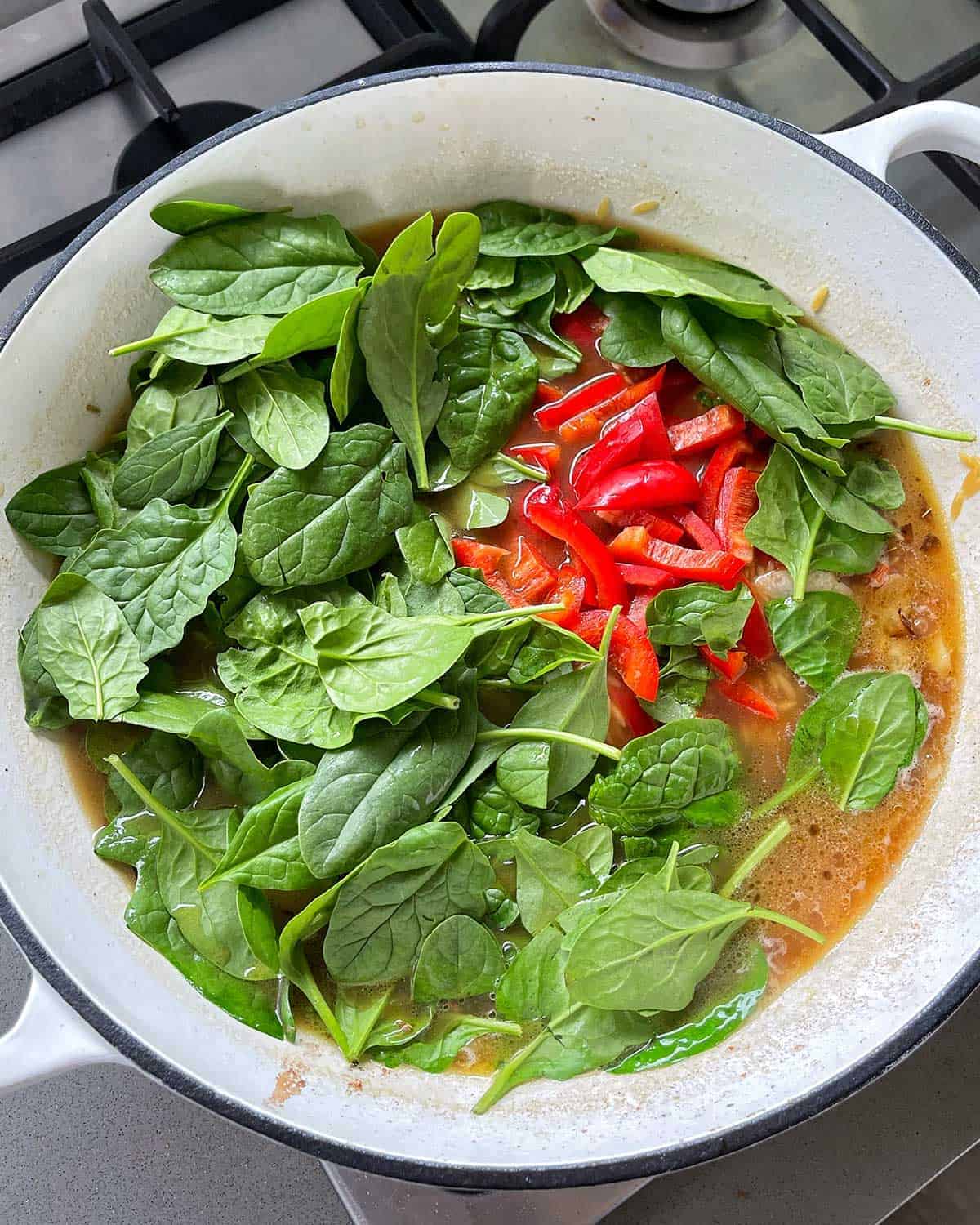 Spinach and capsicum cooking in a large white frying pan.