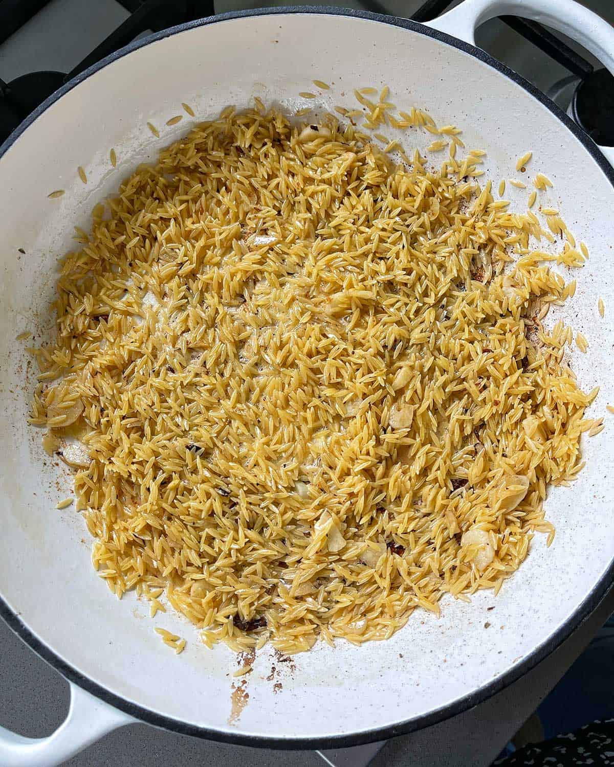 Orzo cooking in a large white frying pan.