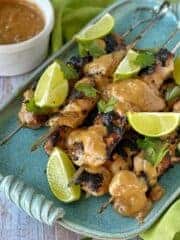 BBQ Satay Chicken Skewers on a blue platter served with lime and coriander.