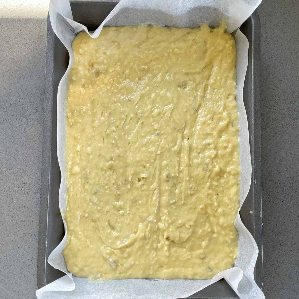 Uncooked banana cake in baking tin sitting on a grey bench