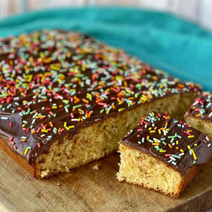 Beautifully cooked banana cake with chocolate icing and colourful sprinkles, cut into slices on a wooden chopping board