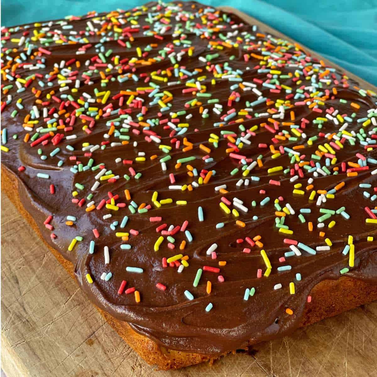 Beautifully cooked banana cake with chocolate icing and colourful sprinkles on a wooden chopping board