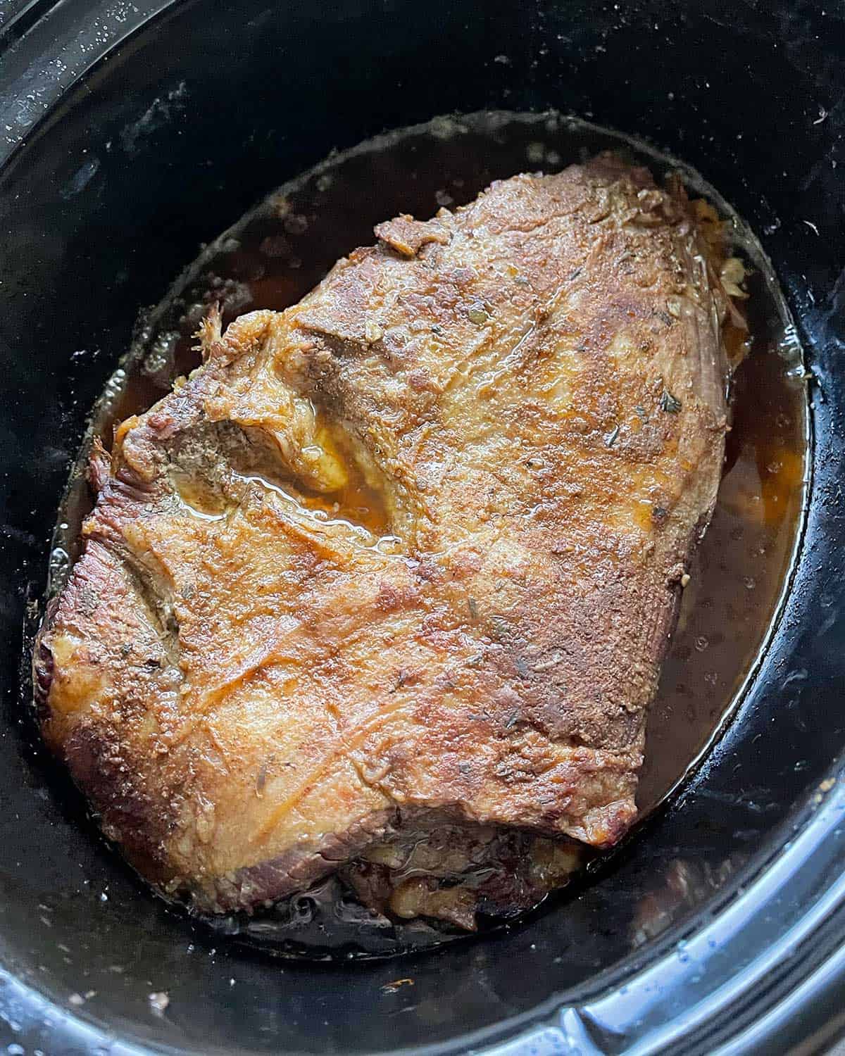 A cooked piece of beef brisket in the base of a slow cooker.