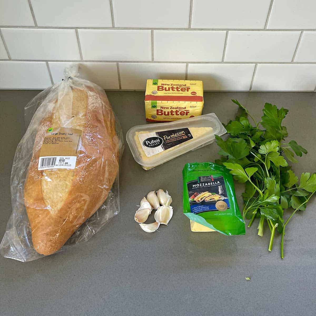 The ingredients for cheesy garlic bread on a grey bench.