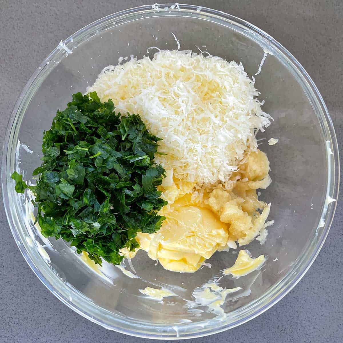 Butter, grated cheese, minced garlic and parsley in a glass bowl.
