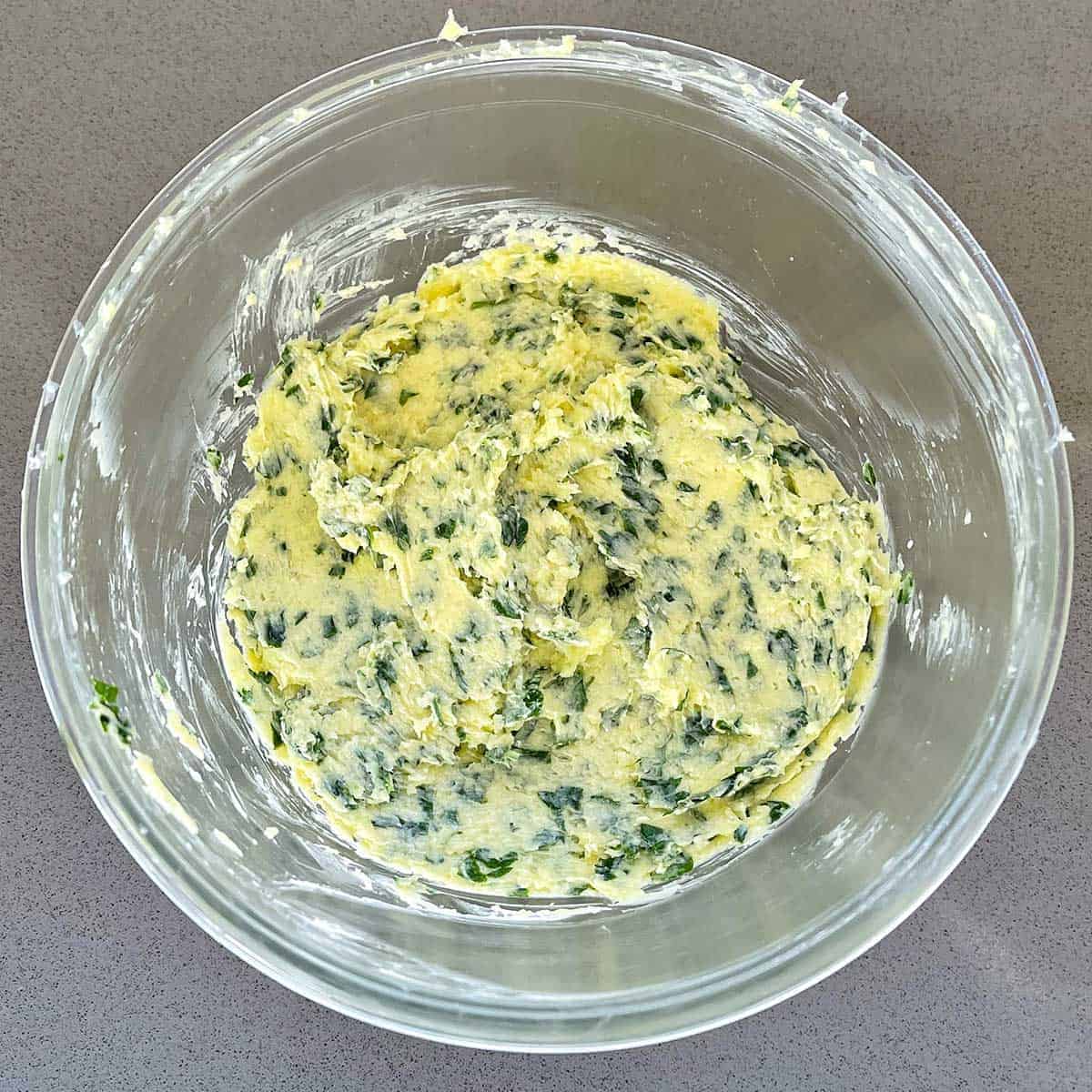 Garlic butter in a glass bowl on a grey bench.