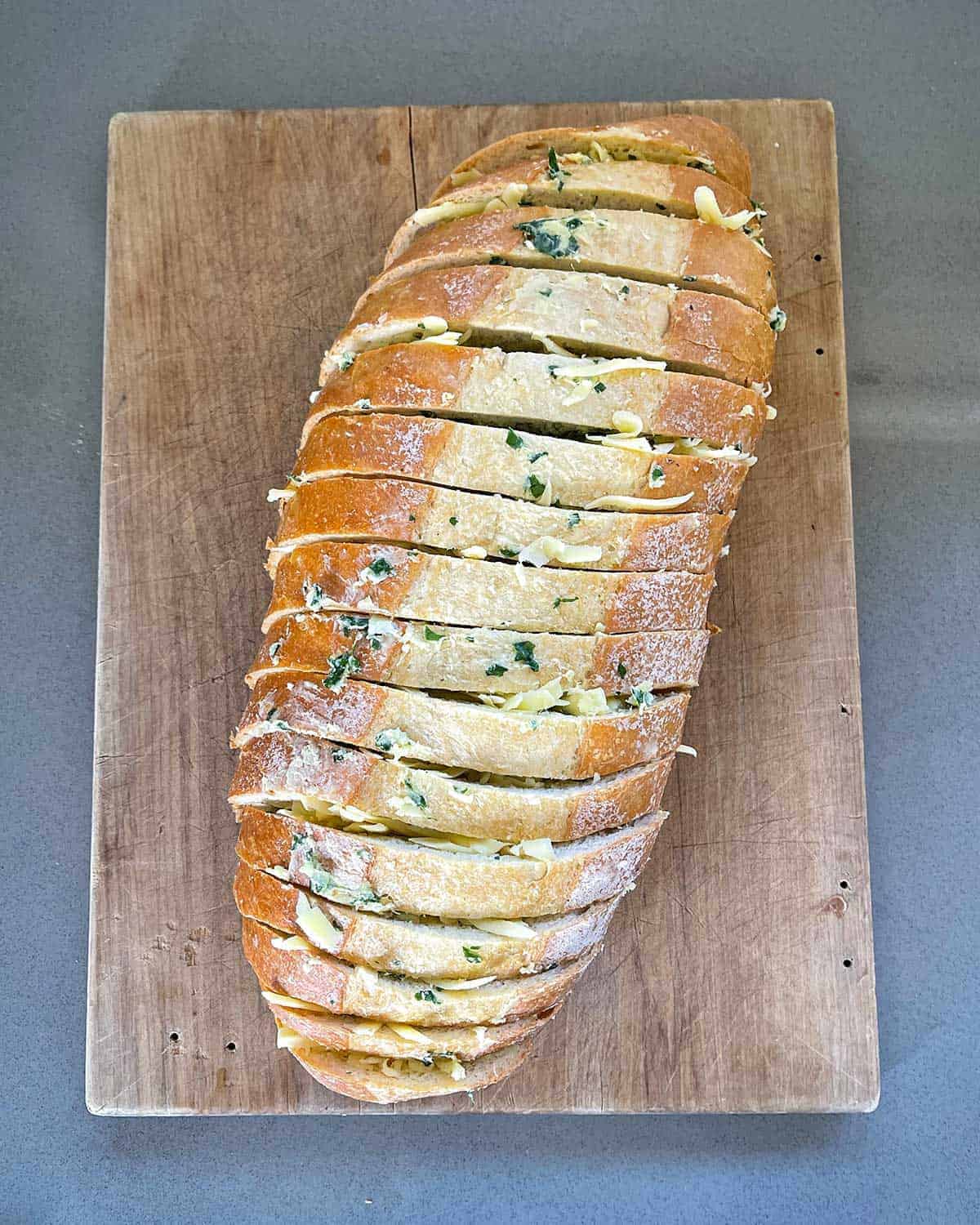 A loaf of sliced garlic bread on a wooden chopping board.