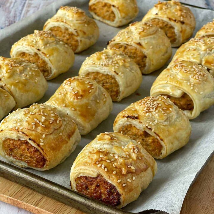 A lined baking tray with cooked chicken sausage rolls.