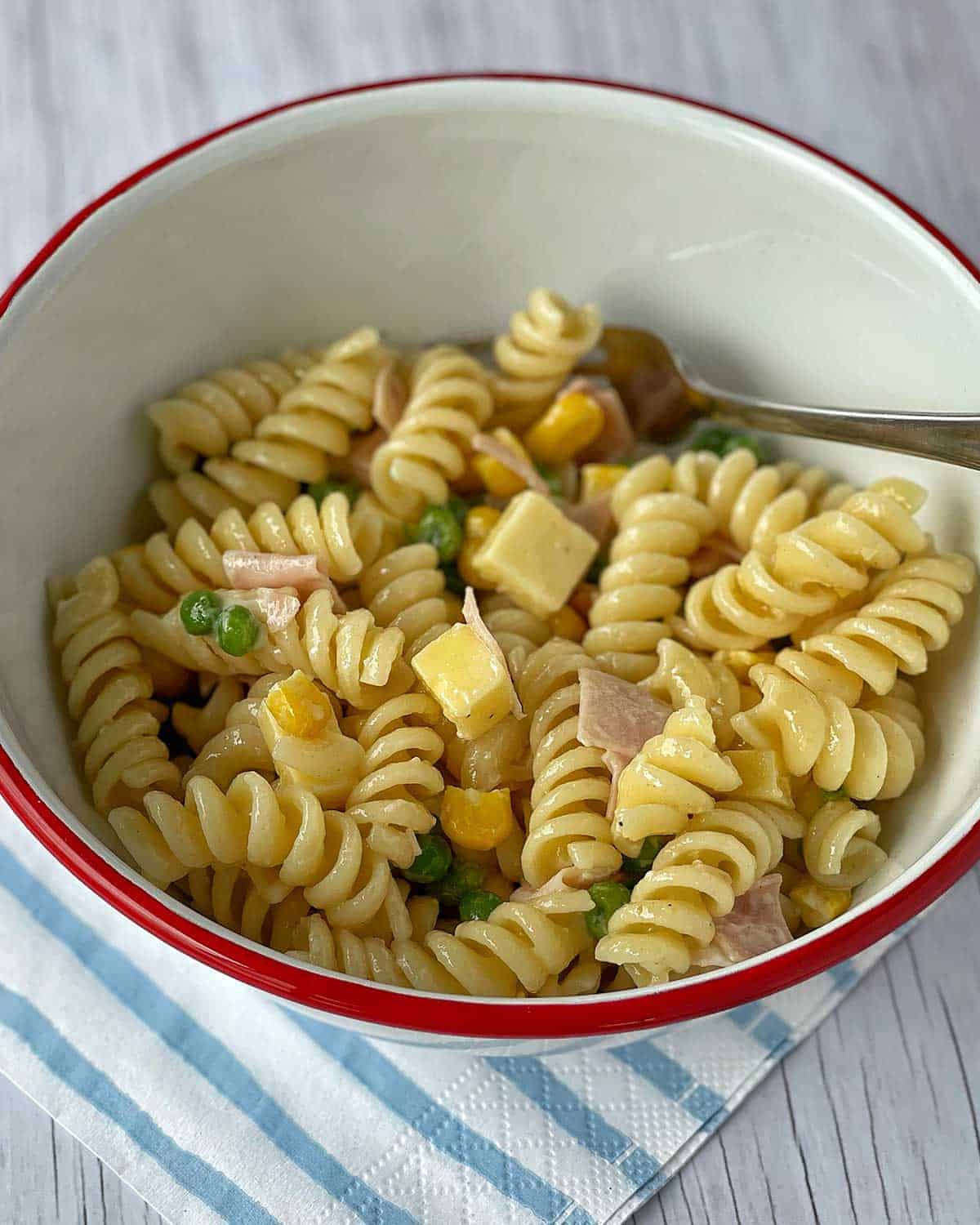 A bowl of Kids' Pasta Salad sitting on a blue and white striped napkin.