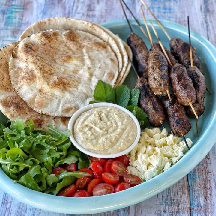 Lamb koftas and salad and wraps on a blue platter.