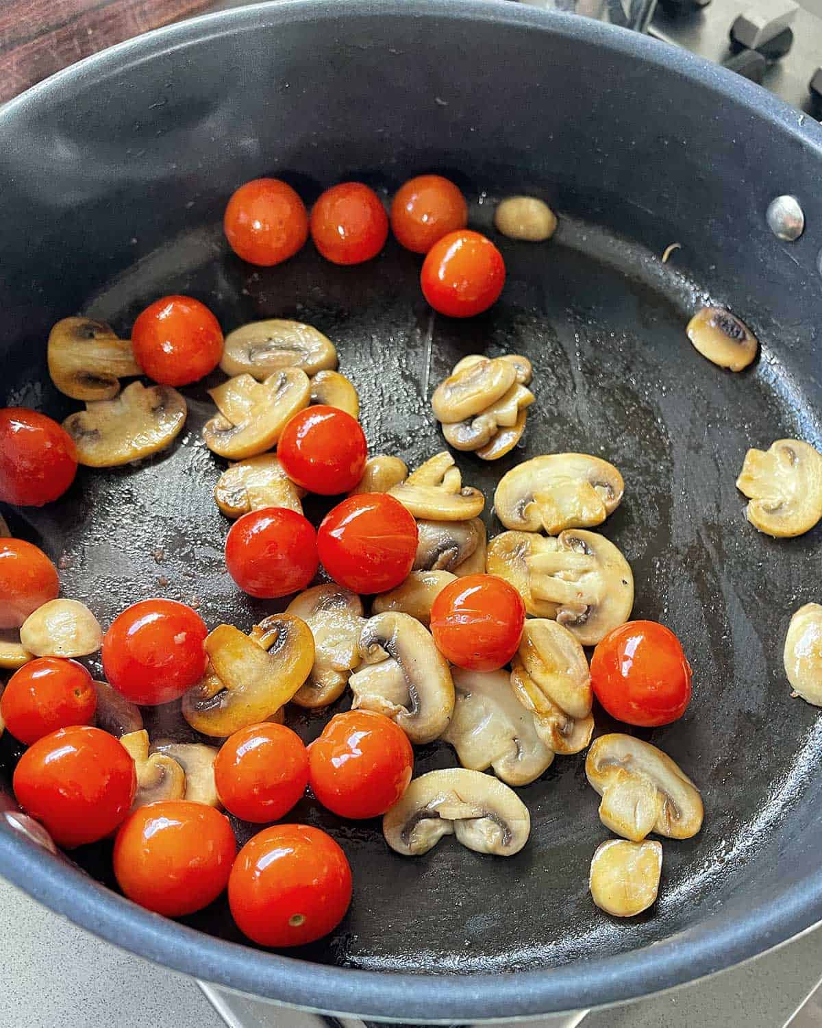 A large frying pan with sliced mushrooms and cherry tomatoes.