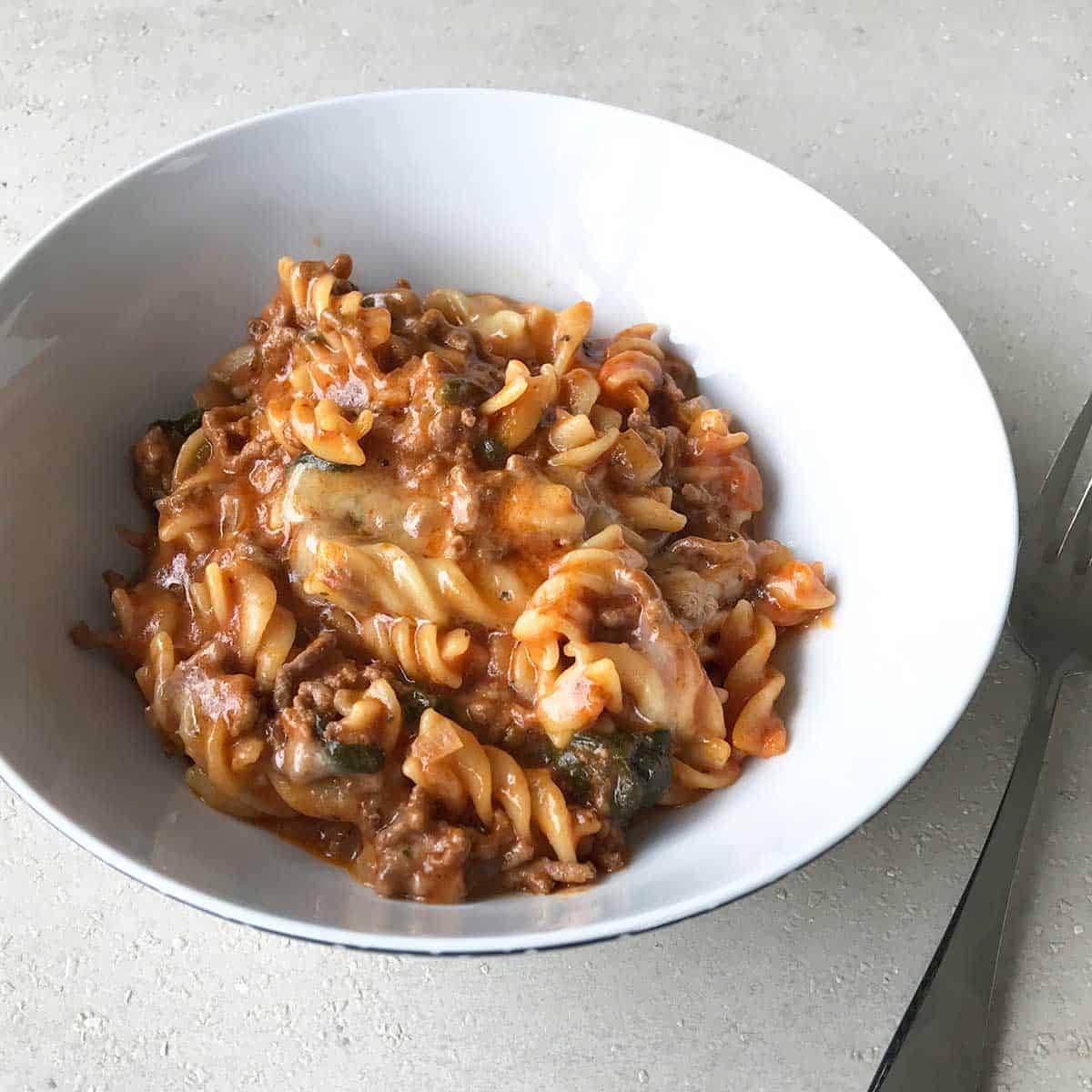 One Pot Mince and Pasta served in a white bowl on a grey bench.