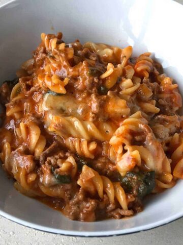 A close up of One Pot Mince and Pasta in a white bowl on a grey bench.