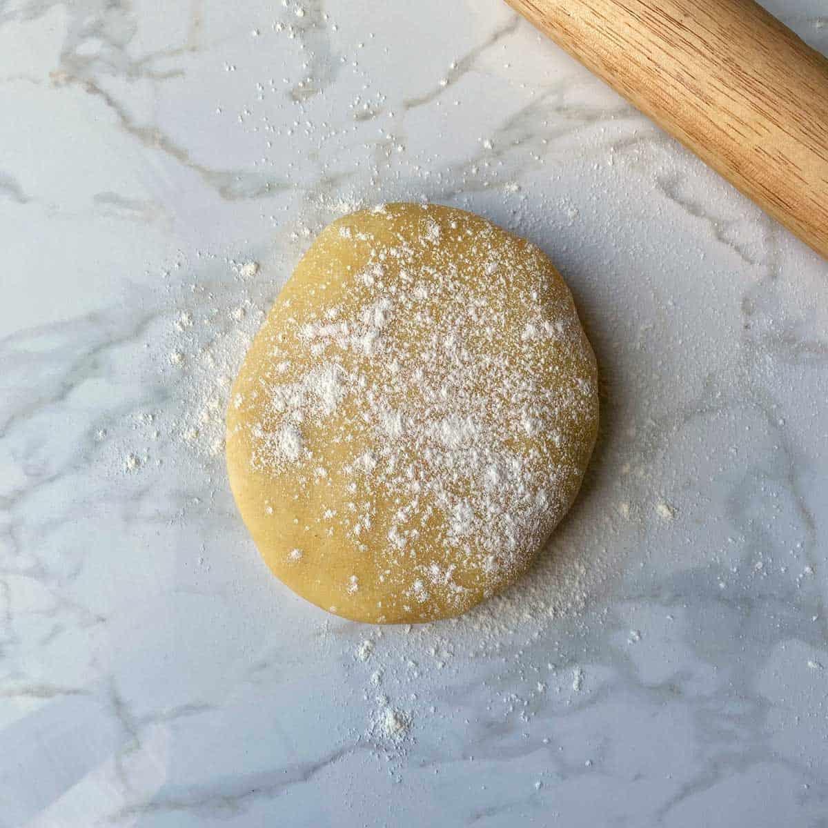 A ball of dough sprinkled with flour next to a rolling pin on a white bench.