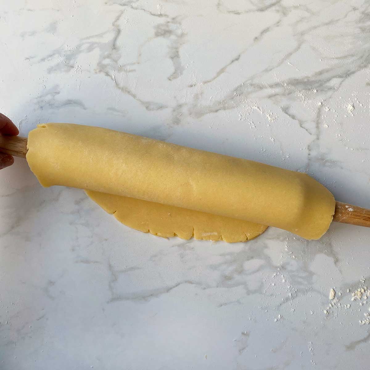 Rolled pastry draped over a rolling pin on a white bench.