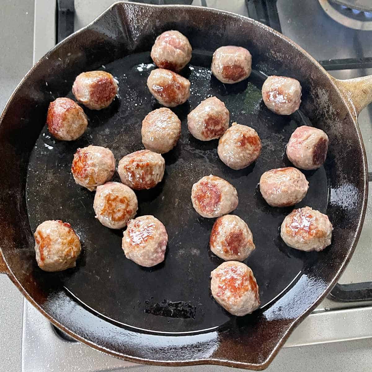 Raw meatballs being cooked until browned in a medium frypan over a medium heat