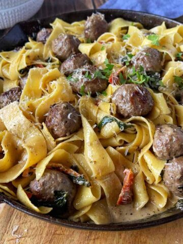 Tuscan meatballs cooked in a medium frypan sitting on a wooden chopping board