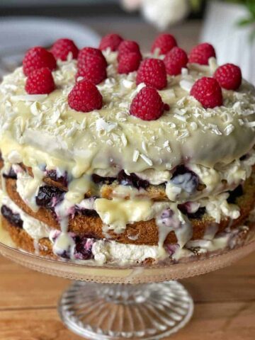 A White Chocolate Cherry Cake sitting on a cake stand.