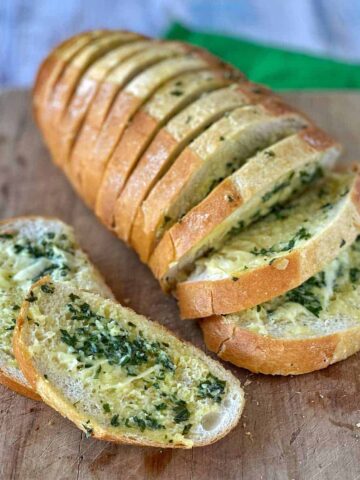 Slices of garlic bread on a wooden chopping board.