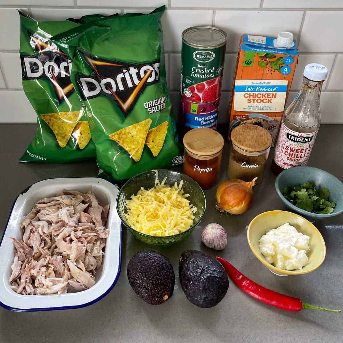 Ingredients for cheesy chicken nachos on a grey bench
