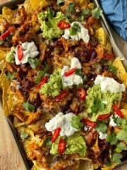 Cheesy chicken nachos served in a baking tray sitting on a wooden chopping board