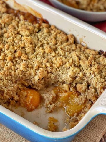 Cooked apricot crumble with a serving taken out sitting on a wooden chopping board