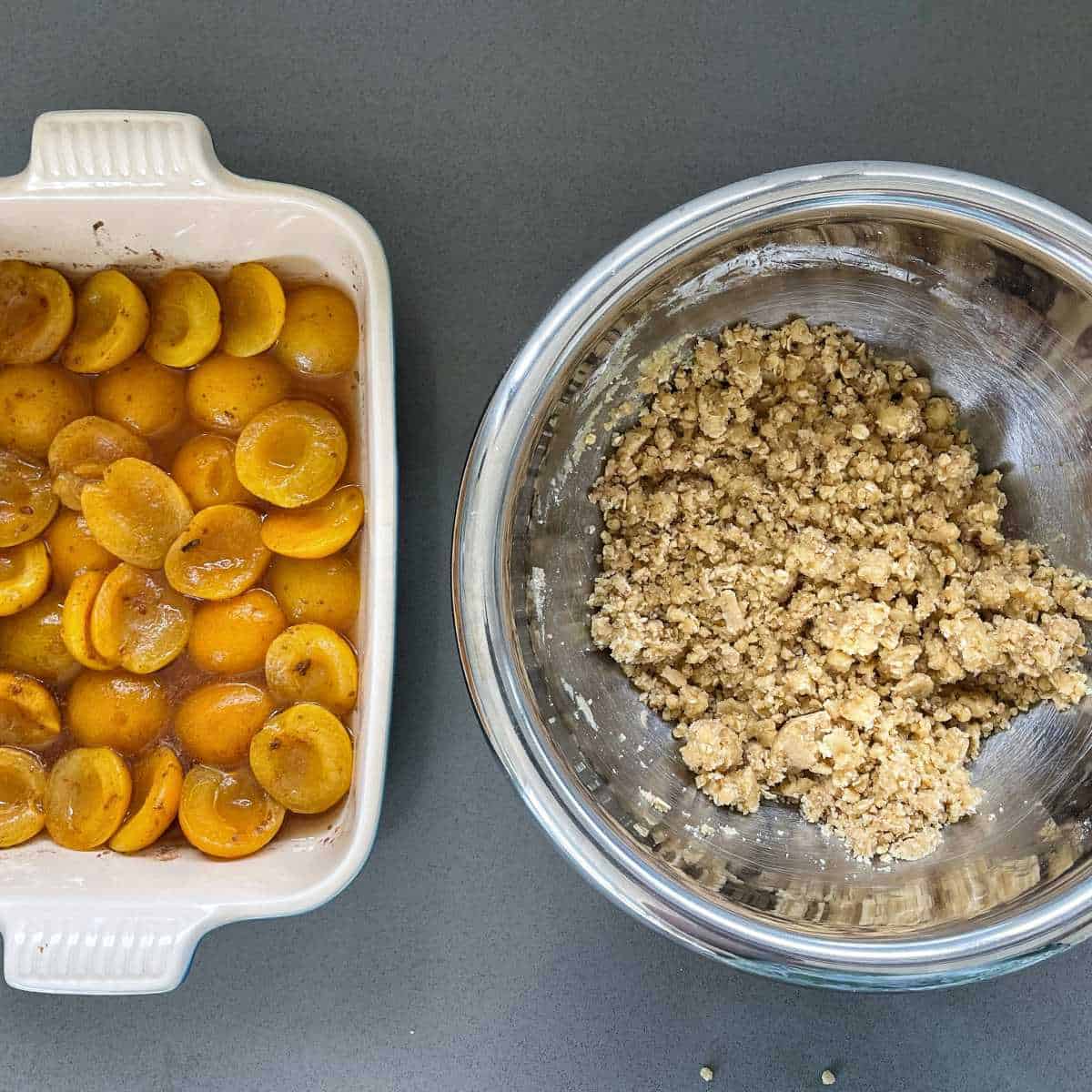 Seasoned apricots and juice sitting beside crumble mix sitting on a grey bench