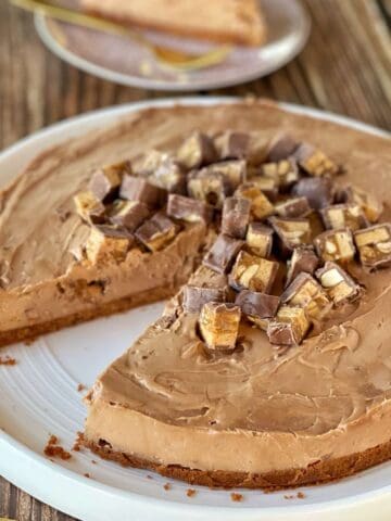 Snickers cheesecake served on a large white plate sitting on a wooden table