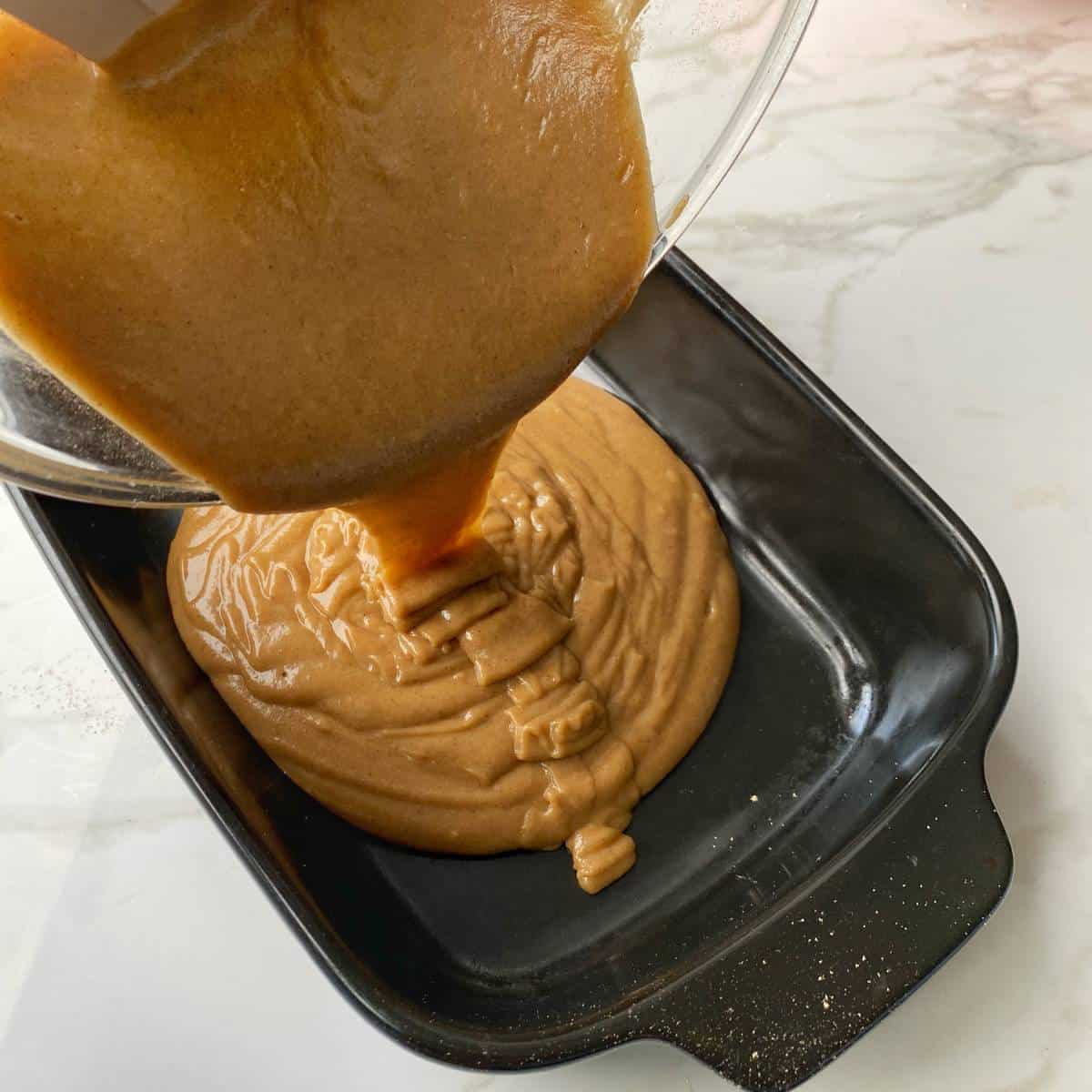 Gingerbread pudding batter being poured from a glass mixing bowl into an oven proof dish