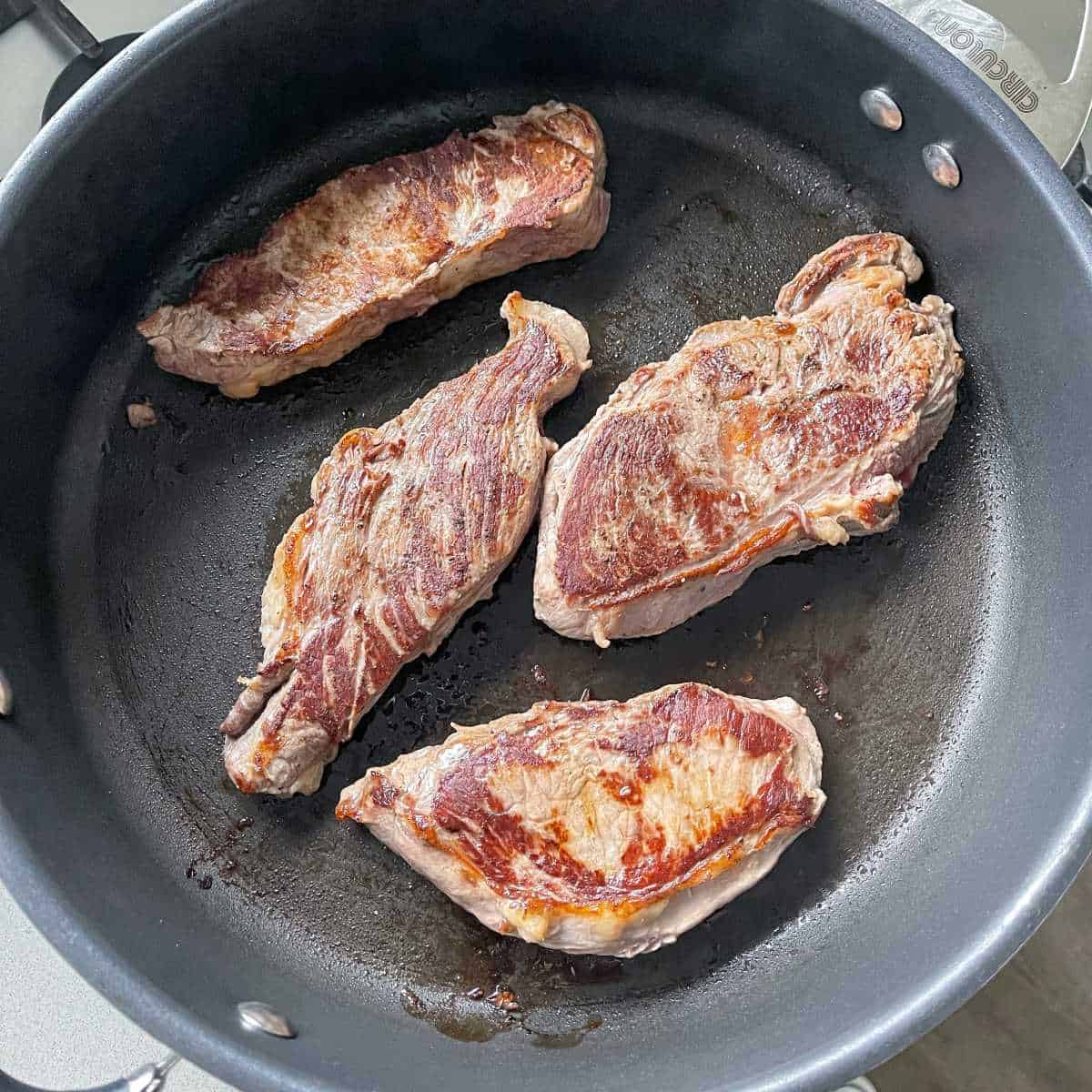 Four pieces of steak frying in a pan