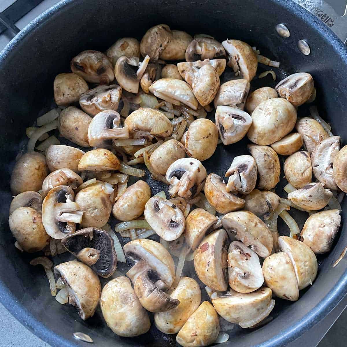 Sliced onion and mushrooms frying in a pan