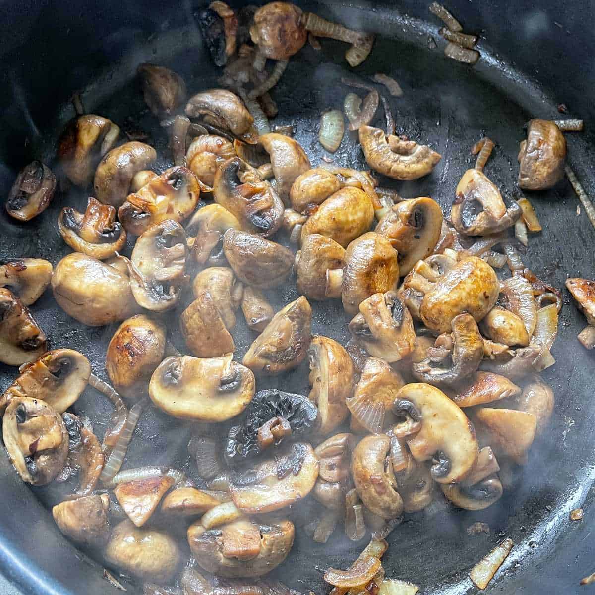 Sliced onion and mushrooms frying in a pan