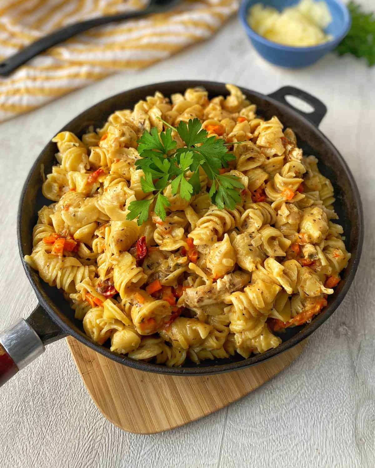 Cheesy chicken pasta all cooked sitting in a fry pan on a wooden chopping board