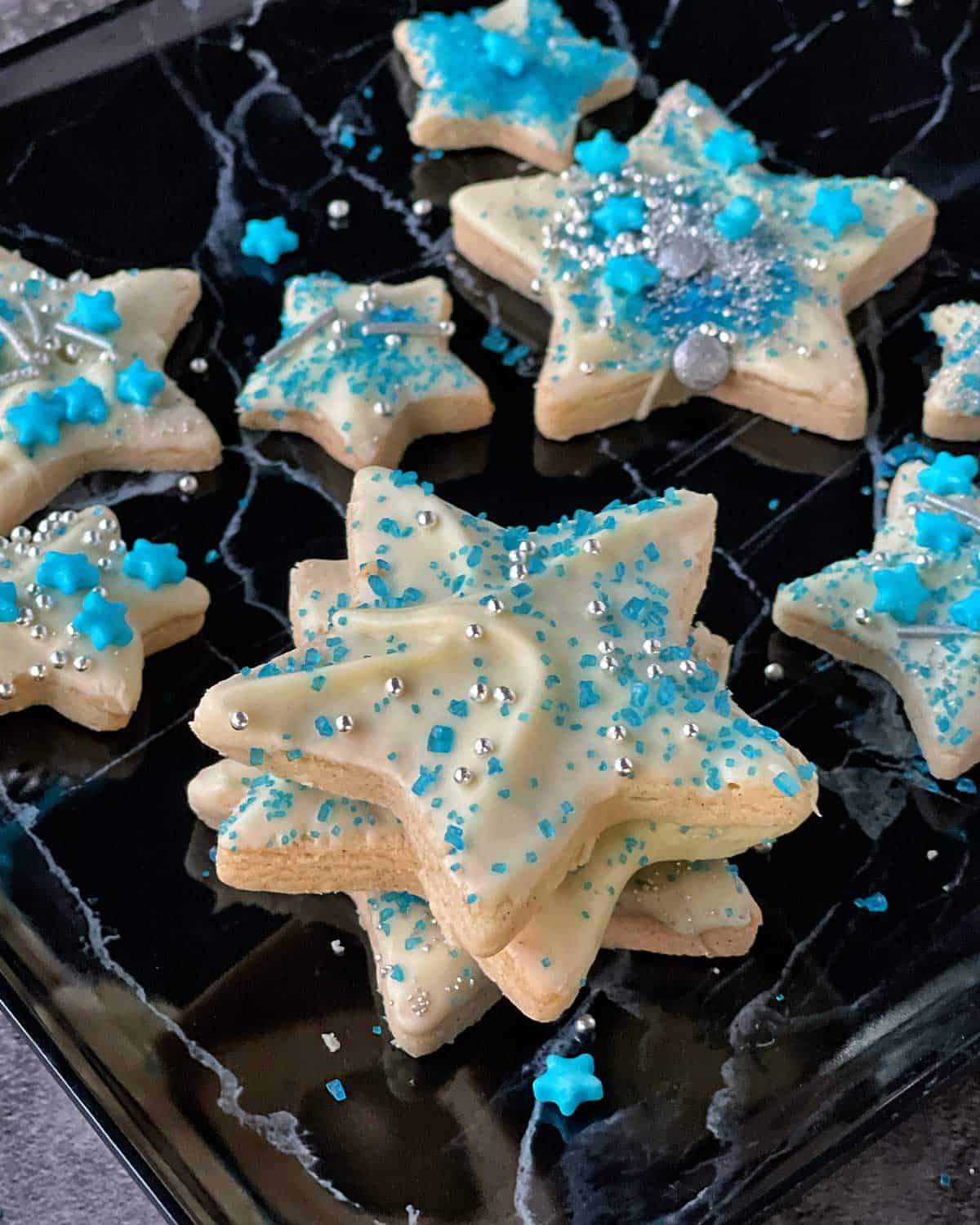 A tray with an assortment of Cinnamon Shortbread Cookies covered in white chocolate and blue sprinkles.