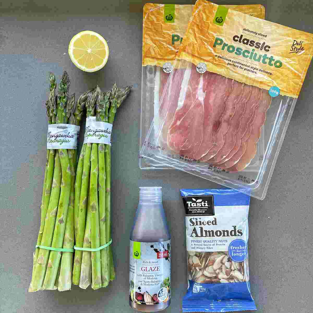 Ingredients for asparagus wrapped in prosciutto sitting on a grey bench top