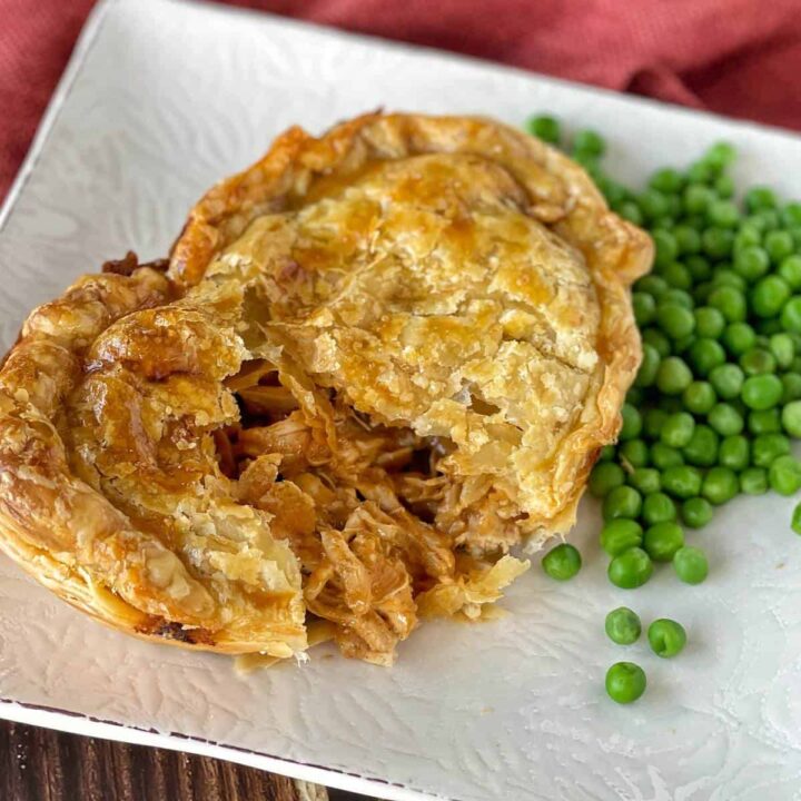 A small butter chicken pie served on a white plate with a side of green peas