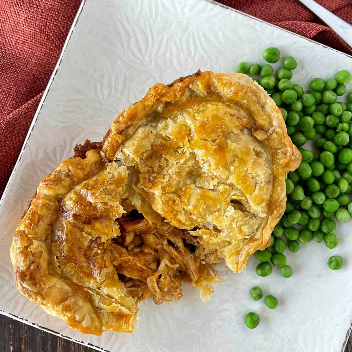 A small butter chicken pie served on a white plate with a side of green peas