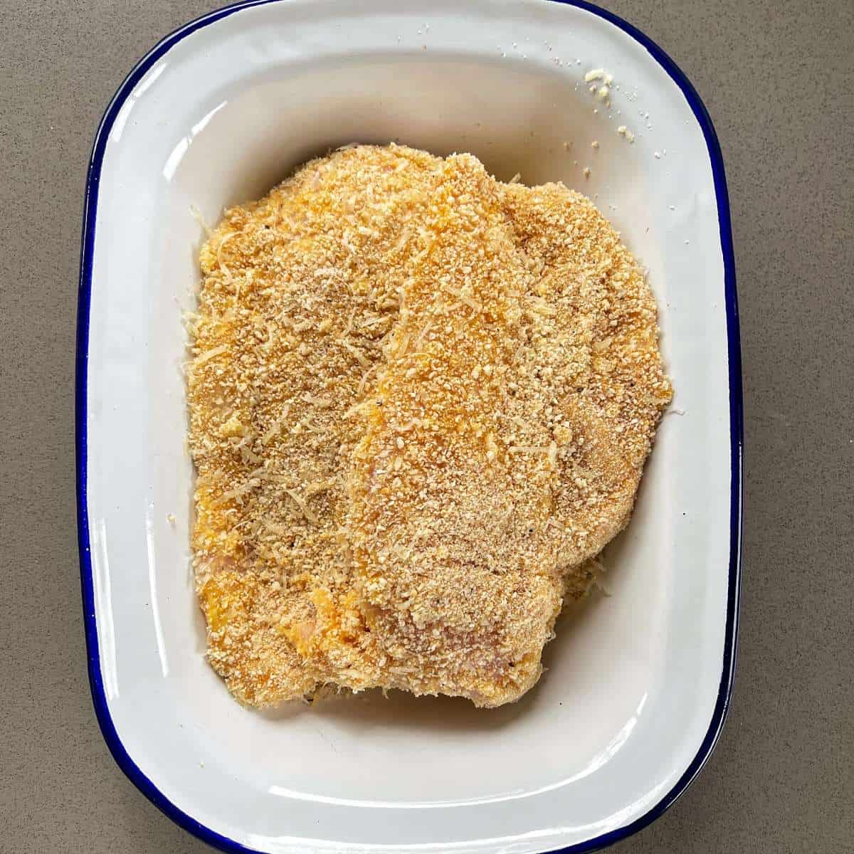 Crumbed chicken breast in a white dish sitting on a grey bench